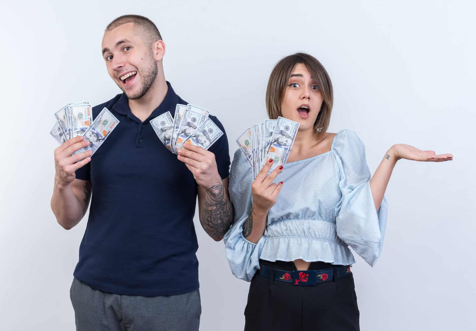 Young Beautiful Couple In Casual Clothes Man And Woman Holding Cash Looking At Camera Smiling Cheerfully Standing Over White Background